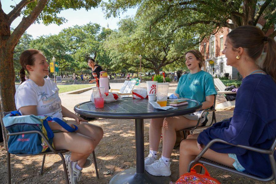 Three female Baylor undergrad students sit around an outdoor table on campus, talking and laughing.